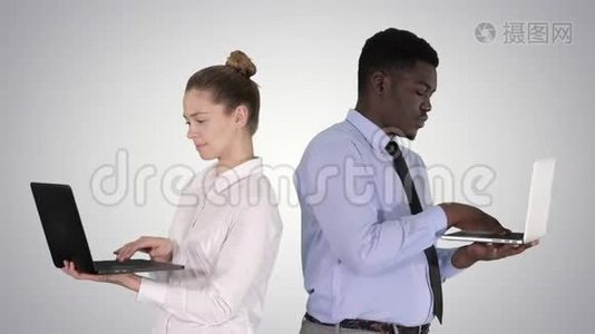 两个背靠背站着，在渐变背景下工作在笔记本电脑上。视频