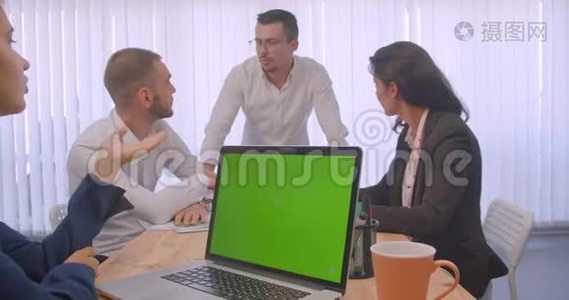 四个大联盟在办公室室内开会的肖像。 商务人士使用带有绿色色屏的笔记本电脑视频