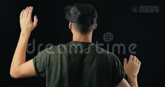 在黑色背景下使用VR眼镜的年轻人肖像。 男性虚拟现实控制台头标玩3D游戏视频