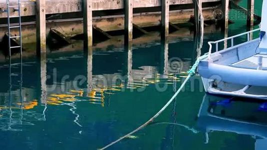 在这段片段中，在平静的水中可以看到有梯子的木墩和用绳子系的小船的倒影视频