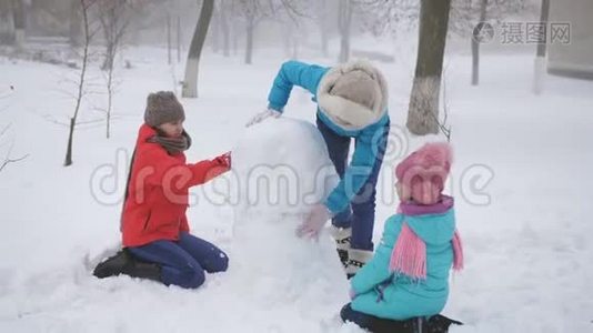 父母和孩子在雪地里玩耍。 妈妈和两个女儿在冬天堆雪人。视频