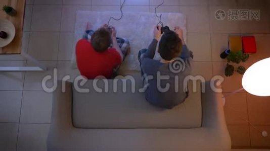 两个穿着睡衣、坐在沙发上和地板上玩游戏的年轻人的顶级镜头。视频