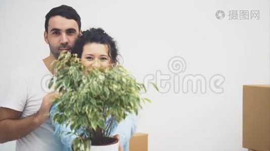 年轻夫妇一起搬到了一间新公寓。 他们拿着一个绿色的花盆，微笑着。 动作，动画。 4K.视频