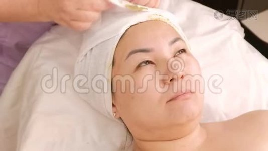 美容师从亚洲女人的头上取下一条毛巾。 在美容中心特写女性的手和脸。 她是视频