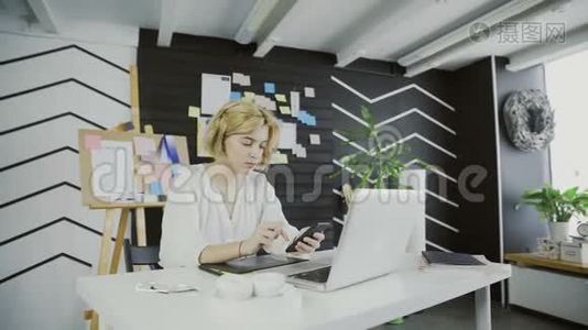 拥有智能手机的漂亮女设计师坐在办公室里视频