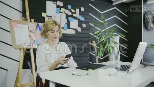 年轻的休闲女士坐在办公桌前，用笔记本电脑，接电话，打电话视频