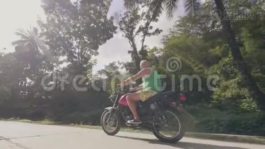 骑摩托车的人骑着摩托车在道路上行驶，绿树成荫。 成熟男人骑摩托车上路视频