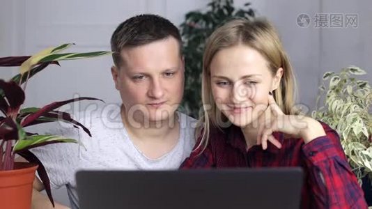 一个年轻人和一个女孩选择了一个新家，坐在笔记本显示器后面视频