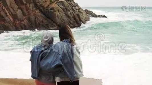 一对女孩夫妇穿着一件夹克，看着美丽的暴风雨海景。视频