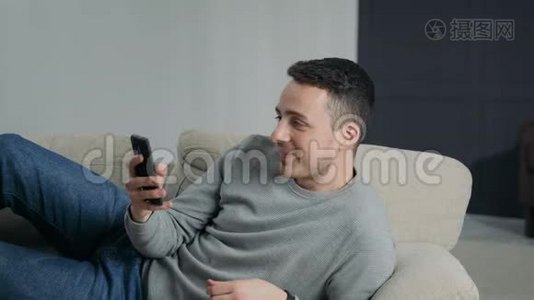 躺在沙发上的男人视频通话智能手机吗？视频