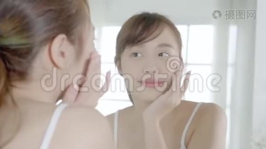 美丽的年轻亚洲女性快乐地将面霜或乳液与保湿剂一起涂抹在皮肤上视频