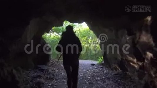 带着背包和手电筒的女游客走出黑暗的洞穴，举起双手，太阳光线视频