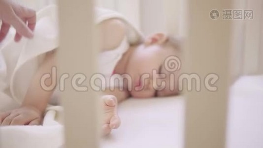 两岁的小女孩睡在铺着白色毯子的婴儿床上。 妈妈给宝宝盖上毯子.. 日间睡眠视频