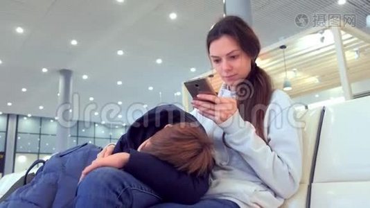 女人带着疲惫的儿子在机场大厅的手机上在线登记。视频