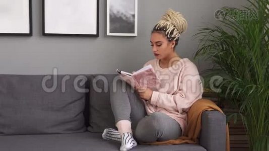 年轻女性坐在舒适的沙发上写着笔记本视频