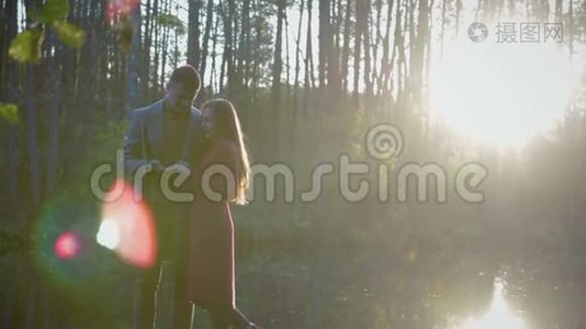 一对浪漫的情侣站在湖边亲吻，他们之间有阳光和阳光视频