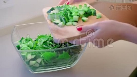 特写镜头，动作缓慢，一个未被认出的女人把切好的黄瓜倒在木板上，放进一个玻璃色拉碗里，碗里有一个大的视频