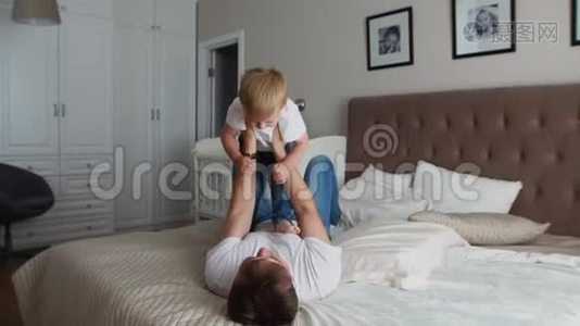 爸爸躺在床上保持尊严. 一个穿着白色T恤的男孩在玩他的游戏时笑了笑视频