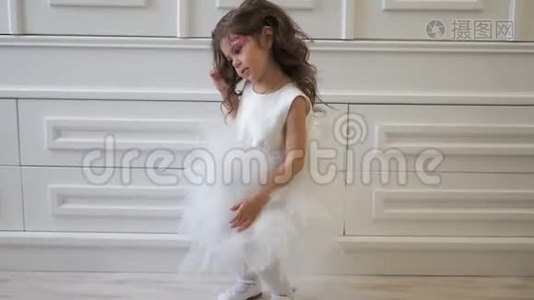 小女孩穿着华丽的白色连衣裙，在室内做着闪亮的化妆和发型，在室内跳舞视频