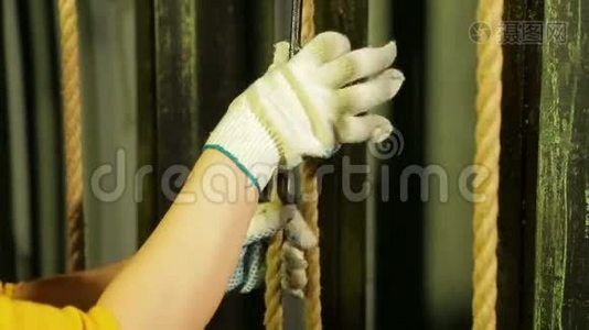 一位年轻的女舞台工作者戴着手套，把坐骑放在一根电缆上的剧院窗帘的升降机构上。视频
