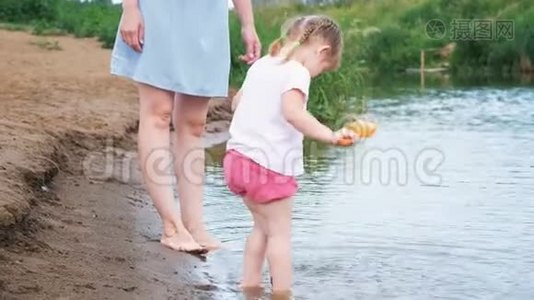 小孩子在河里玩，夏天女孩从锅里倒水。 妈妈照顾她的女儿。视频