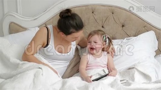 可爱的小女孩有两个马尾辫正在床上哭泣。 母亲正试图让女儿在卧室里平静下来。视频