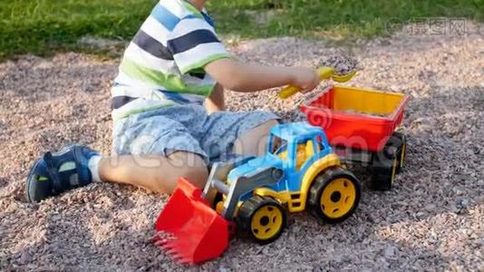 用塑料铲子在玩具拖车里装砾石的小男孩特写4k视频视频