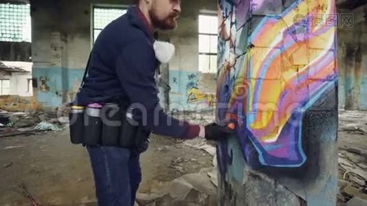 在旧建筑内破损的柱子上画涂鸦的有创意留胡子的家伙的倾斜镜头视频