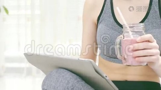 年轻女子正在喝冰沙，并在她的平板电脑上使用健身应用程序。视频