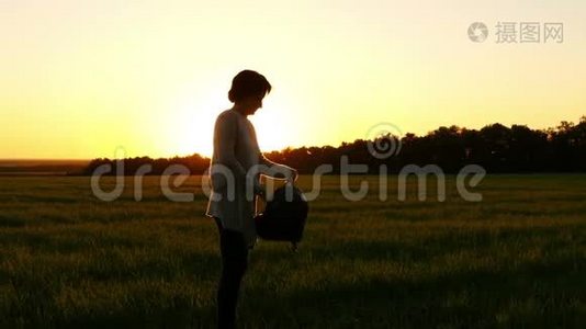 一个女孩穿着背包，在夕阳的背景下沿着一片绿色的草坪，动作缓慢视频