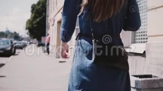 后视年轻女性时尚博主身穿蓝色长裙，留着长发，时尚包包在街上慢条斯理地走着。视频