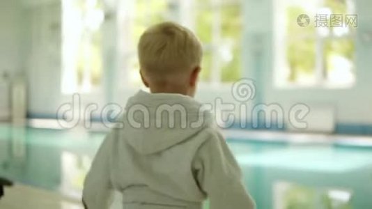 一个穿着浴袍的小男孩从两只手中把球扔进游泳池的背面。 很好玩。 在外面视频
