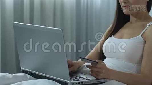 年轻女子在笔记本电脑上输入信用卡号码，坐在床上，在网上购物视频