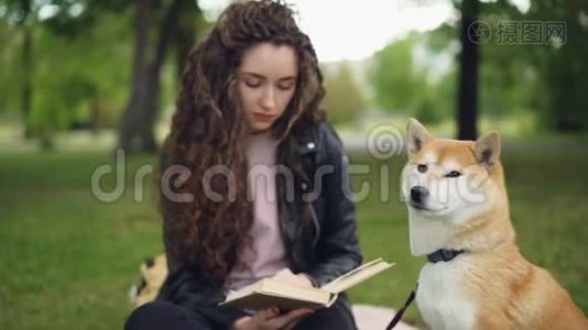 可爱的学生正在看书，坐在公园里，然后拍拍可爱的小狗，微笑着。 可爱的动物，聪明的视频
