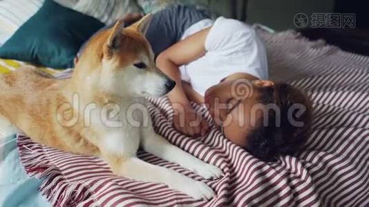 一位迷人的非洲裔美国女士正睡在木制床上，床上铺着现代亚麻布，而她可爱的忠实狗则躺在她身边视频