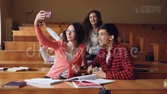 快乐的学生正在教室里自拍，坐在桌子旁，拿着智能手机。 现代技术视频
