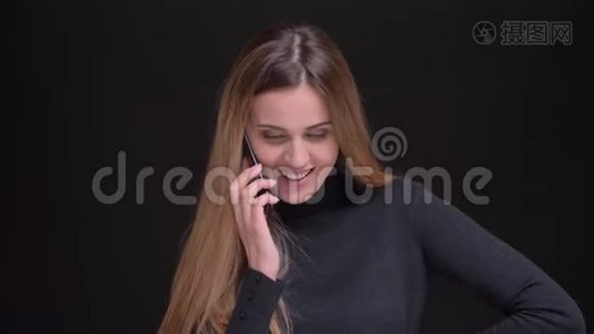 年轻的白种人长发金发金发女孩在黑色背景下用手机微笑交谈的肖像。视频