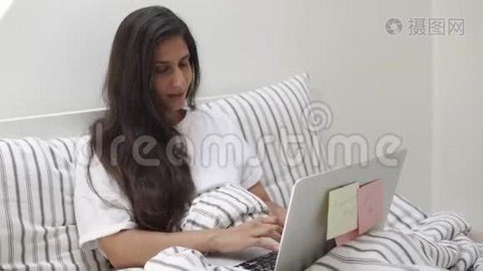 年轻漂亮的女人正在房间里的床上用笔记本电脑打字视频