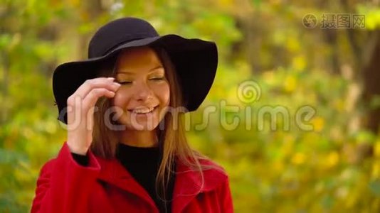 秋天森林中一个美丽的微笑女孩戴着一顶黑色帽子，前景是一片黄色的枫叶视频