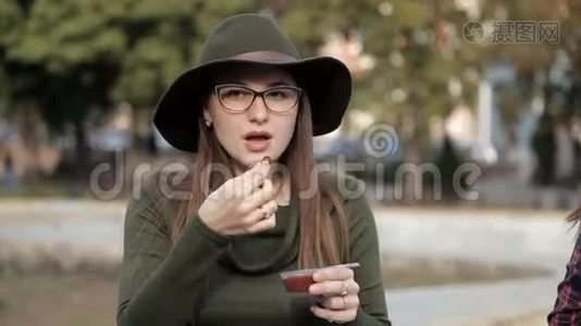 一个年轻的女孩坐在公园里，正在尝试一种美味的酱汁。 散步，吃饭视频