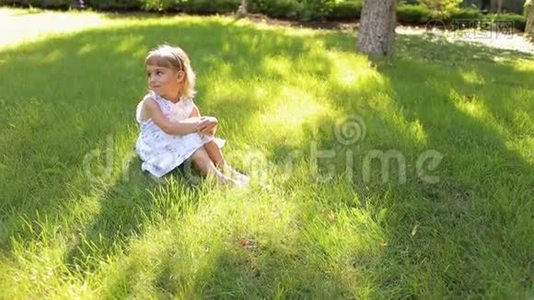 一个可爱的小女孩坐在公园的草地上，肖像。视频