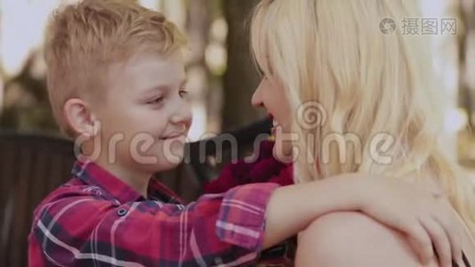 美丽的小男孩在公园里的长凳上给他心爱的母亲一束花。视频