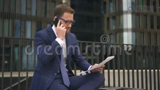 一位穿着蓝色西装的自信商人在电话中谈论他手上的文件视频