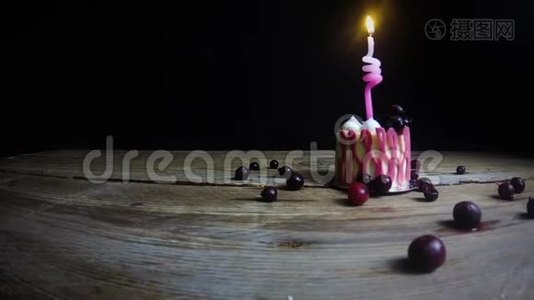 一支燃烧着的蜡烛在一张老式木桌上的一个喜庆的粉红色纸杯蛋糕上燃烧着。 手拿起蜡烛。 在黑色的视频