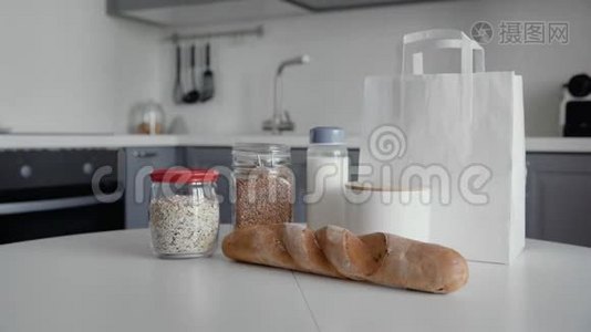 厨房木制桌子上有面包、燕麦片、荞麦、牛奶、蔬菜的未包装购物袋。 零垃圾家庭和视频