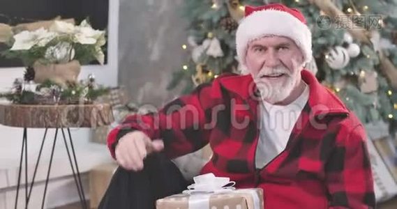 英俊的高白种人坐在新年树的背景下，挥手交谈的肖像。 快乐圣诞老人视频