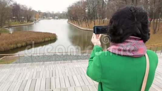 秋天阴天女人在公园里拍池塘的照片从后面看视频