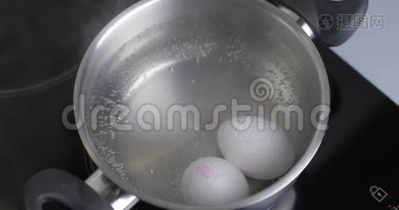 两个生的白鸡蛋在不锈锅中煮在沸水中。 健康的天然蛋白质早餐烹饪。 鸡蛋是视频