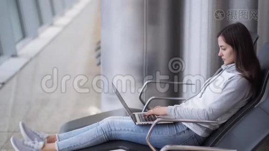 年轻女子坐在候机室，用笔记本电脑在机场工作视频