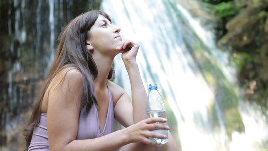 女人在瀑布旁用塑料瓶喝水视频